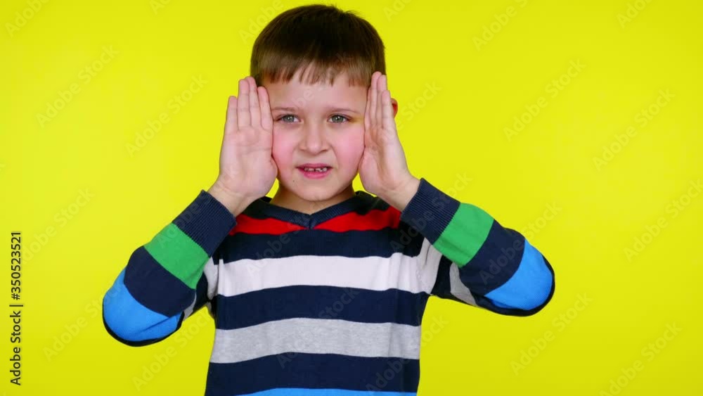 Funny little child boy in a multi-colored sweater takes his hands off his face and smiles on a yellow background with copy space. Place for text or product. 4K slowmotion footage Funny little child boy in a multi-colored sweater takes his hands off his face and smiles on a yellow background with copy space. Place for text or product. 4K slowmotion footage
