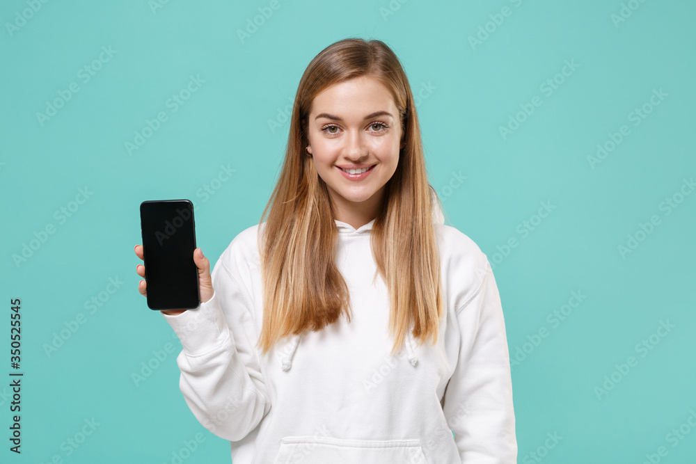 Smiling young woman girl in casual white hoodie posing isolated on blue turquoise background studio portrait. People lifestyle concept. Mock up copy space. Hold mobile phone with blank empty screen. Smiling young woman girl in casual white hoodie posing isolated on blue turquoise background studio portrait. People lifestyle concept. Mock up copy space. Hold mobile phone with blank empty screen.