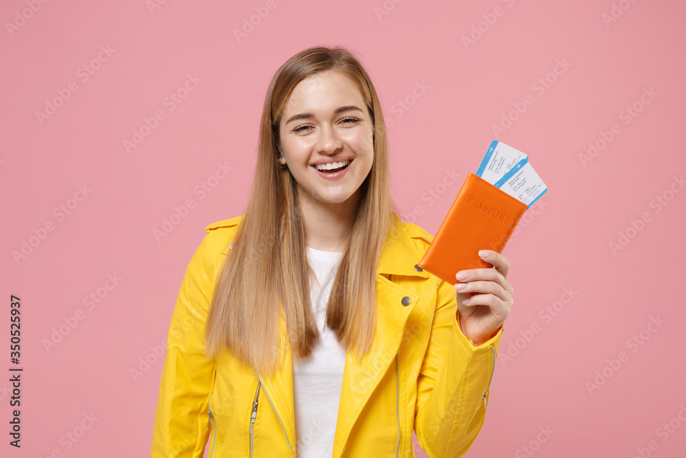 Smiling young woman girl in yellow leather jacket posing isolated on pastel pink wall background studio portrait. People lifestyle concept. Mock up copy space. Hold passport tickets boarding pass. Smiling young woman girl in yellow leather jacket posing isolated on pastel pink wall background studio portrait. People lifestyle concept. Mock up copy space. Hold passport tickets boarding pass.