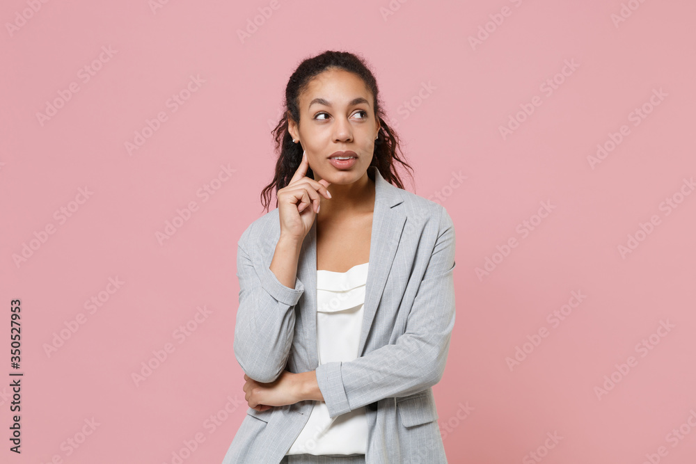 Pensive young african american business woman in grey suit, white shirt isolated on pink background studio. Achievement career wealth business concept. Mock up copy space. Put hand prop up on chin. Pensive young african american business woman in grey suit, white shirt isolated on pink background studio. Achievement career wealth business concept. Mock up copy space. Put hand prop up on chin.