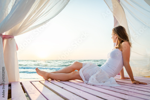 Woman in white dress relaxing on the beah. Sunrise