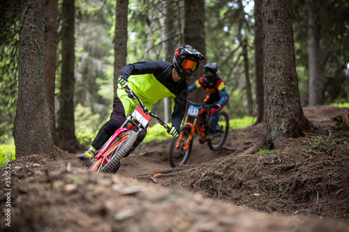 Man and young woman on mountain bikes rides on trails trough the forest. 
