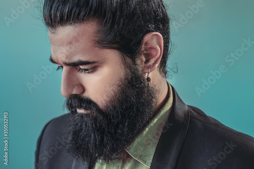 close up side view of bearded man with a man bun hairstyle posing in a studio wearing a suit and earrings whilst looking down, male model fashion portrait photograph