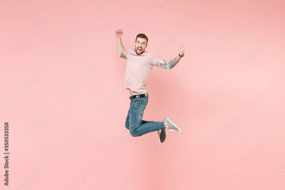 Obraz premium Side view of excited young tattooed man guy in pastel casual t-shirt posing isolated on pink background. People lifestyle concept. Mock up copy space. Jumping, doing winner gesture, looking camera.