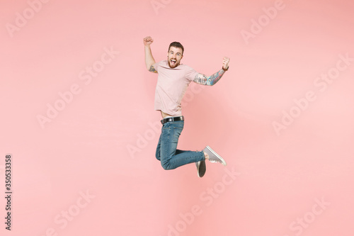 Side view of excited young tattooed man guy in pastel casual t-shirt posing isolated on pink background. People lifestyle concept. Mock up copy space. Jumping, doing winner gesture, looking camera. © ViDi Studio