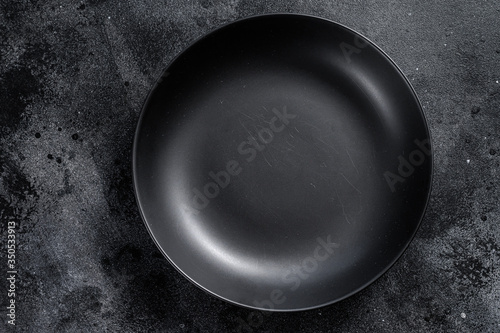 Black plate on textured black background.  Top view. Copy space