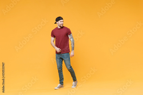 Cheerful young tattooed man guy in casual t-shirt black cap posing isolated on yellow wall background studio portrait. People sincere emotions lifestyle concept. Mock up copy space. Looking aside.