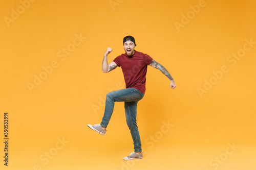 Excited young bearded tattooed man guy in casual t-shirt black cap posing isolated on yellow background studio portrait. People emotions lifestyle concept. Mock up copy space. Doing winner gesture.