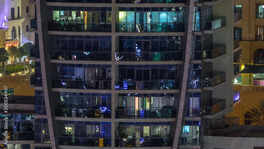 Rows of glowing windows with people in the interior of apartment building with balconies at night. Modern skyscraper with glass surface. Concept for business and modern life Rows of glowing windows with people in the interior of apartment building with balconies at night. Modern skyscraper with glass surface. Concept for business and modern life