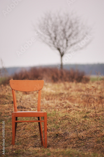 Red vintage, rustic, wooden chair in a field in early spring.