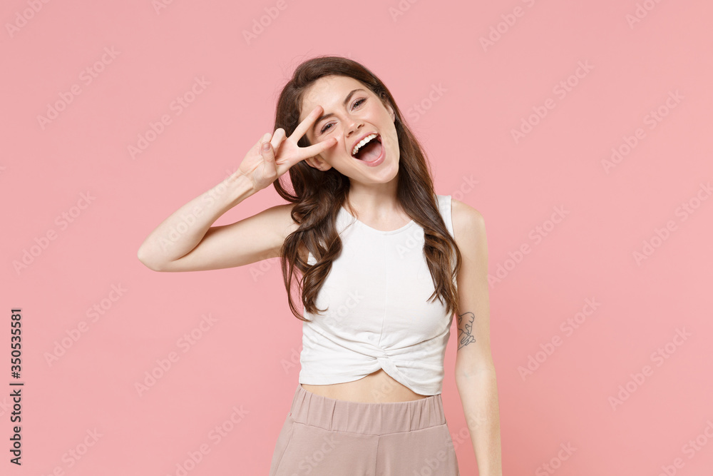 Cheerful young brunette woman girl in light casual clothes posing isolated on pastel pink wall background studio portrait. People emotions lifestyle concept. Mock up copy space. Showing victory sign. Cheerful young brunette woman girl in light casual clothes posing isolated on pastel pink wall background studio portrait. People emotions lifestyle concept. Mock up copy space. Showing victory sign.