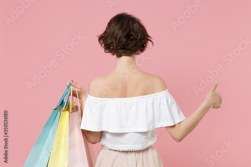 Back rear view of young woman girl in summer clothes hold package bag with purchases isolated on pink background studio portrait. Shopping discount sale concept. Mock up copy space. Showing thumb up.