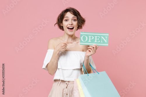 Excited young woman girl in summer clothes isolated on pink background. Shopping discount sale concept. Mock up copy space. Hold package bag with purchases point index finger on sign with OPEN title.
