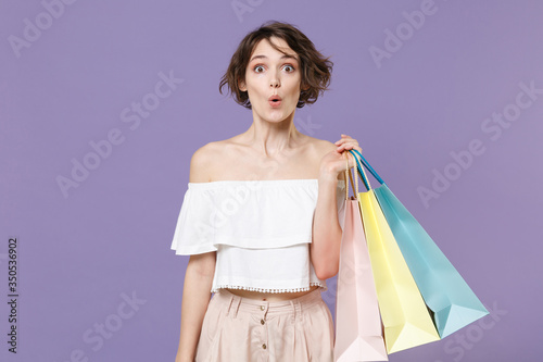 Shocked young woman girl in summer clothes hold package bag with purchases isolated on pastel violet background studio portrait. Shopping discount sale concept. Mock up copy space. Looking camera.