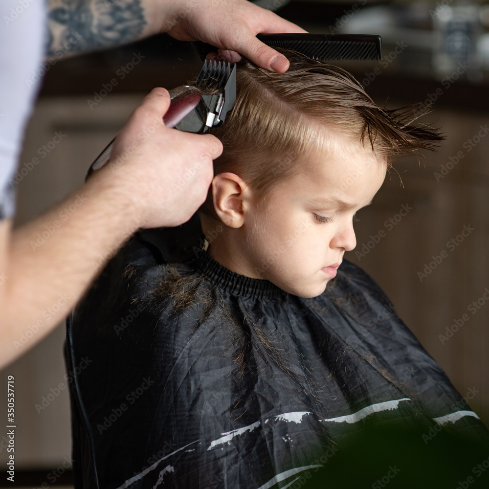 Fototapeta premium Barbershop and hairdressing at home. Men's and children's haircuts. The hairdresser cuts the boy. Stylish hairstyle for a child