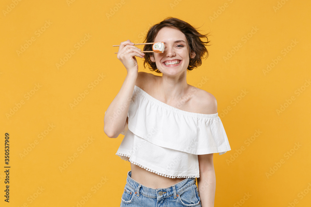 Young brunette woman girl in casual clothes hold in hand sticks chopsticks with makizushi sushi roll traditional japanese food isolated on yellow background studio portrait. People lifestyle concept. Young brunette woman girl in casual clothes hold in hand sticks chopsticks with makizushi sushi roll traditional japanese food isolated on yellow background studio portrait. People lifestyle concept.