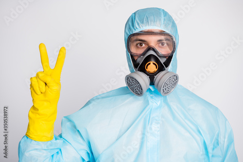 Portrait of medical worker man in white hazmat uniform breathing mask make v-sign isolated over gray color background