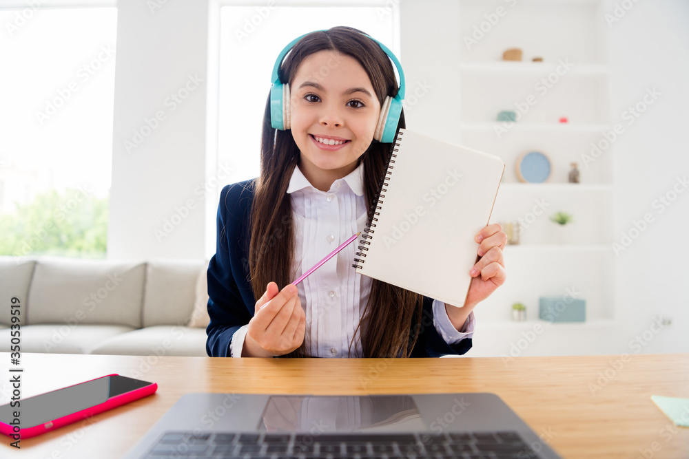 Closeup photo of little student lady talk skype notebook online lesson video call sit desk showing teacher copybook homework done tasks use earphones distance quarantine living room indoors Closeup photo of little student lady talk skype notebook online lesson video call sit desk showing teacher copybook homework done tasks use earphones distance quarantine living room indoors