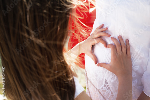 Close-up of the preteen girl hends in heart on the abdomen belly photo