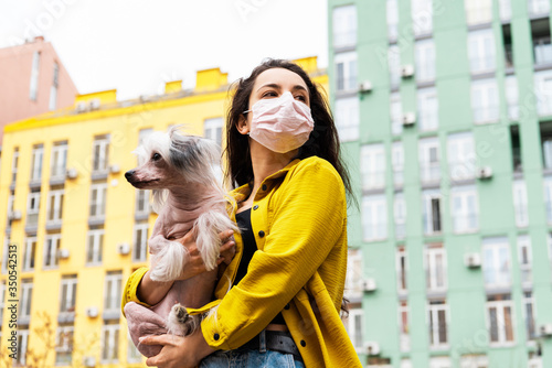 attractive girl in pink medical mask walking with dog in city