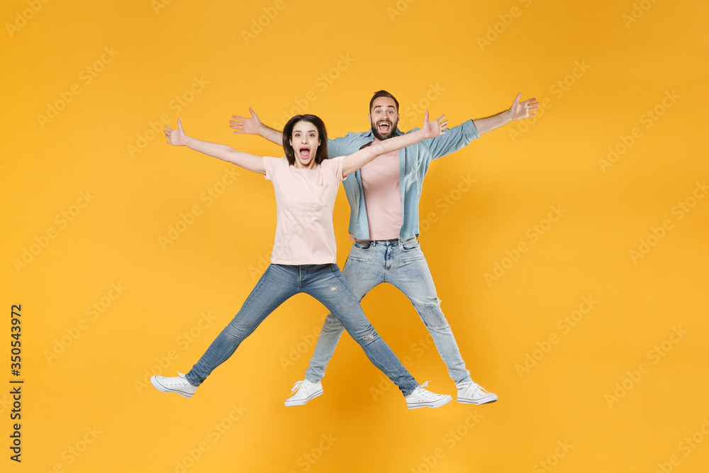 Excited young couple two friends guy girl in pastel blue casual clothes posing isolated on yellow background in studio. People lifestyle concept. Mock up copy space. Jumping, spreading hands and legs.