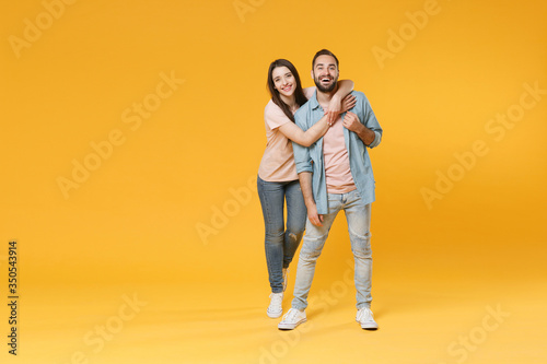 Funny young couple two friends guy girl in pastel blue casual clothes posing isolated on yellow wall background studio portrait. People lifestyle concept. Mock up copy space. Hugging, looking camera.