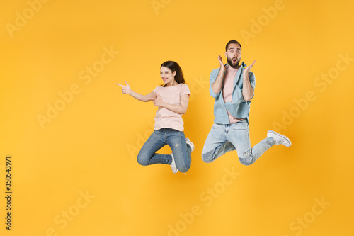 Funny shocked couple friends guy girl in pastel blue casual clothes isolated on yellow background. People lifestyle concept. Mock up copy space. Jumping pointing index fingers aside spreading hands.