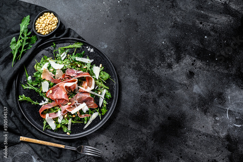 Salad with Parma, prosciutto ham, arugula and Parmesan. Black background, top view, space for text