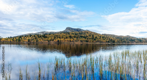 Beautiful and calm autumn colored landscape scenery early morning in Norway, mountain reflects in the water.