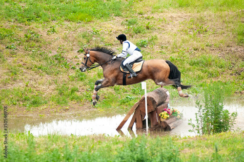 Eventing: equestrian rider jumping over an a log fence water obstacle