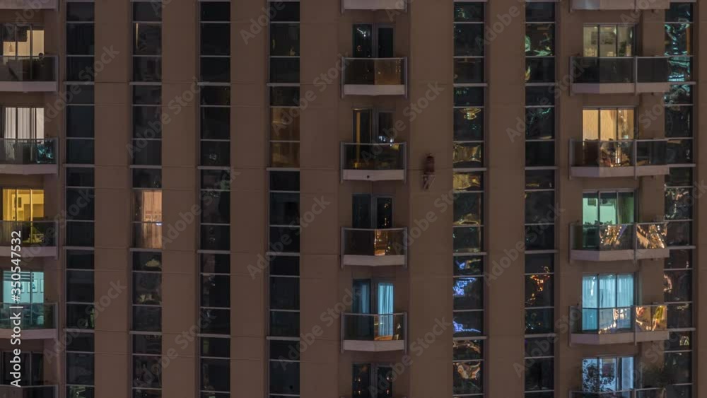Rows of glowing windows with people in the interior of apartment building at night. Modern skyscraper in the city. Concept for business and modern life