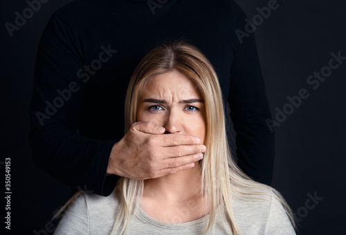 фотографія Man hand is cover mouth of despaired scared girl, with black silhouette behind