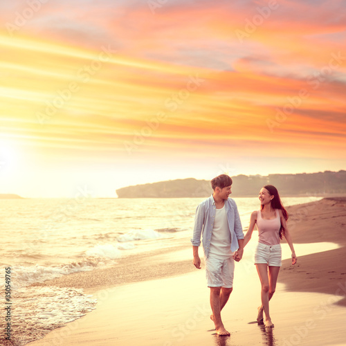 happy asian young couple walking on the beach at sunset