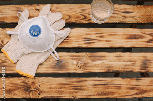 Mask, gloves are lying on the wooden table background. Glass of water is standing on the wooden background. Safety.