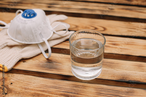 Mask, gloves are lying on the wooden table background. Glass of water is standing on the wooden background. Safety.