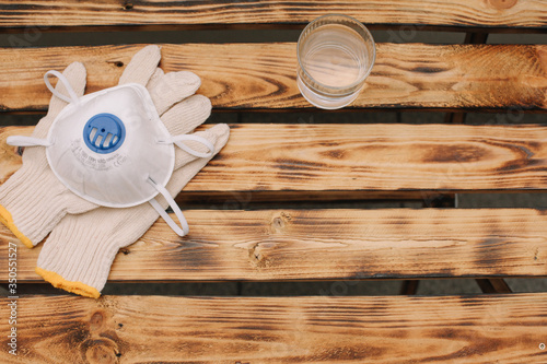 Mask, gloves are lying on the wooden table background. Glass of water is standing on the wooden background. Safety.