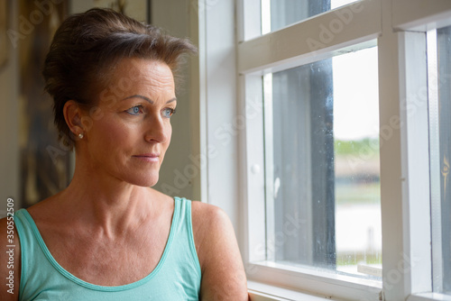 Face of mature beautiful woman looking outside the window