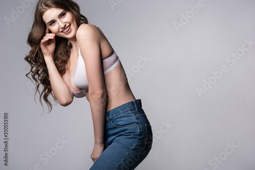 happy woman in bra and jeans standing isolated on grey