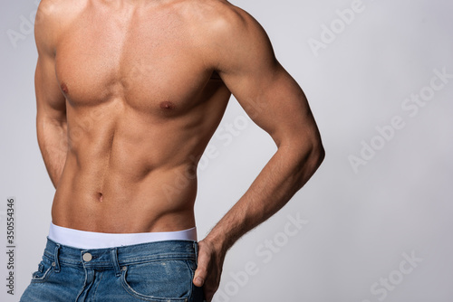 cropped view of shirtless and muscular man in denim jeans isolated on grey