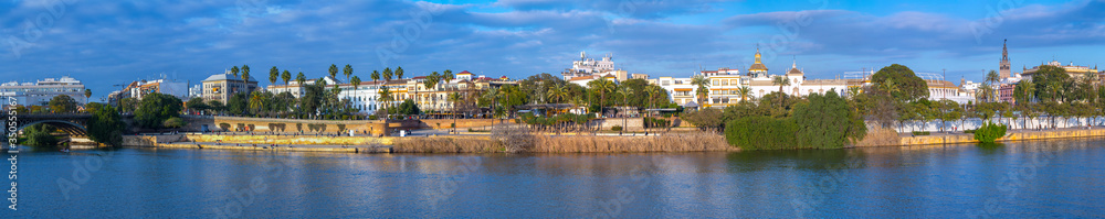 Panoramic view of the waterfront of the Guadalquivir River in Seville, Andalusia, Spain. On a warm winter evening, people relax and stroll along the waterfront.