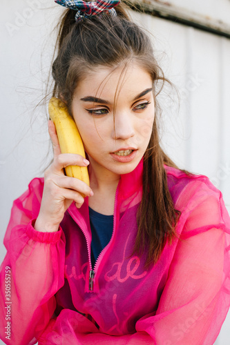Model girl talking on banana in pink blouse posing in garages. Street style trendy portraites
