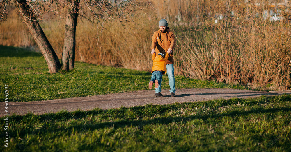 Father and daughter playing in park on green grass. Father's day. Little girl plays with dad outside. Father circling daughter holding hands.