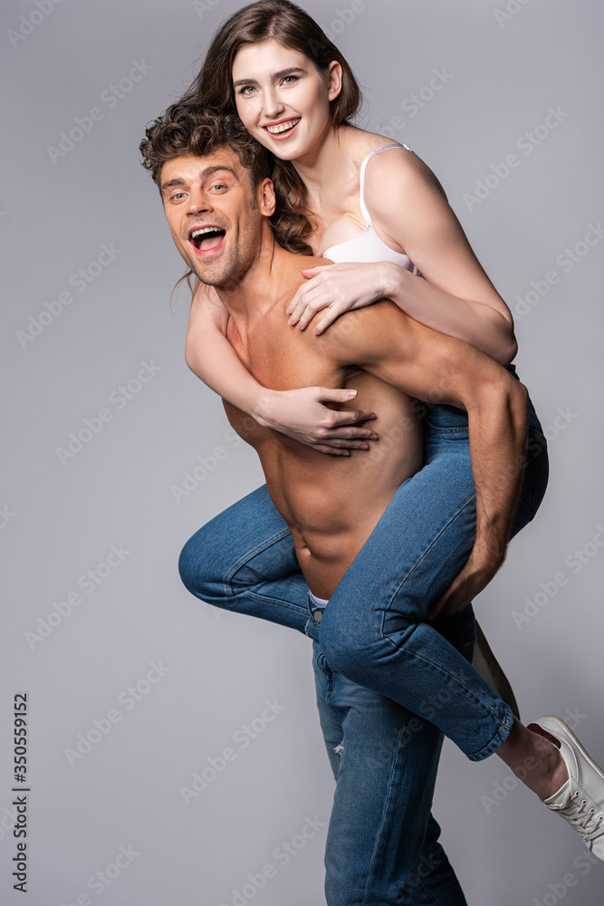excited and muscular man piggybacking happy girlfriend on grey excited and muscular man piggybacking happy girlfriend on grey
