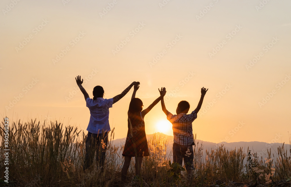 Silhouette of three children playing with raised hands on the mountain at the sunset time.