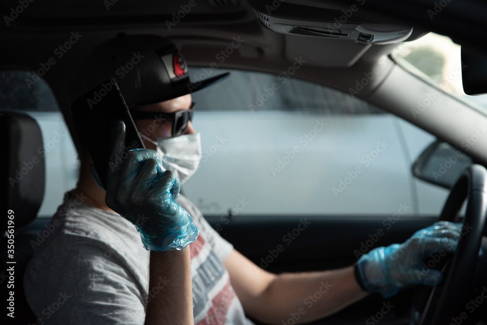 A young man siiting in the medical mask and protective gloves inside the car. Remedies and social distancing. Life during the epidemic of coronavirus. Safety measures during the delivery services. A young man siiting in the medical mask and protective gloves inside the car. Remedies and social distancing. Life during the epidemic of coronavirus. Safety measures during the delivery services.