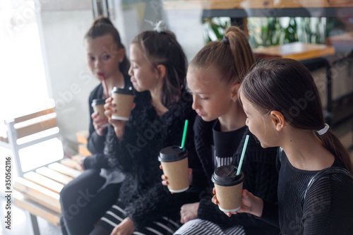 Group of female preteen kids  communicate together outdoor and drinking warm coffee drink in takeaway paper glasses