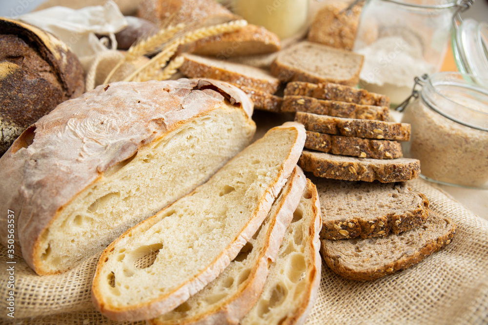 Closeup of wheat and whole grain slices, cut loafs and baguettes, sackcloth and flour in jar. Bakery or traditional bread concept