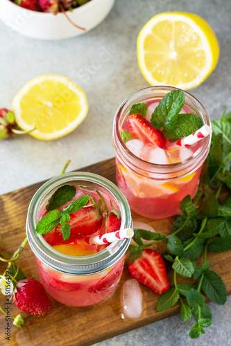 Summer drink refreshing. Lemonade with fresh strawberries, ice and lemons on a light stone countertop.