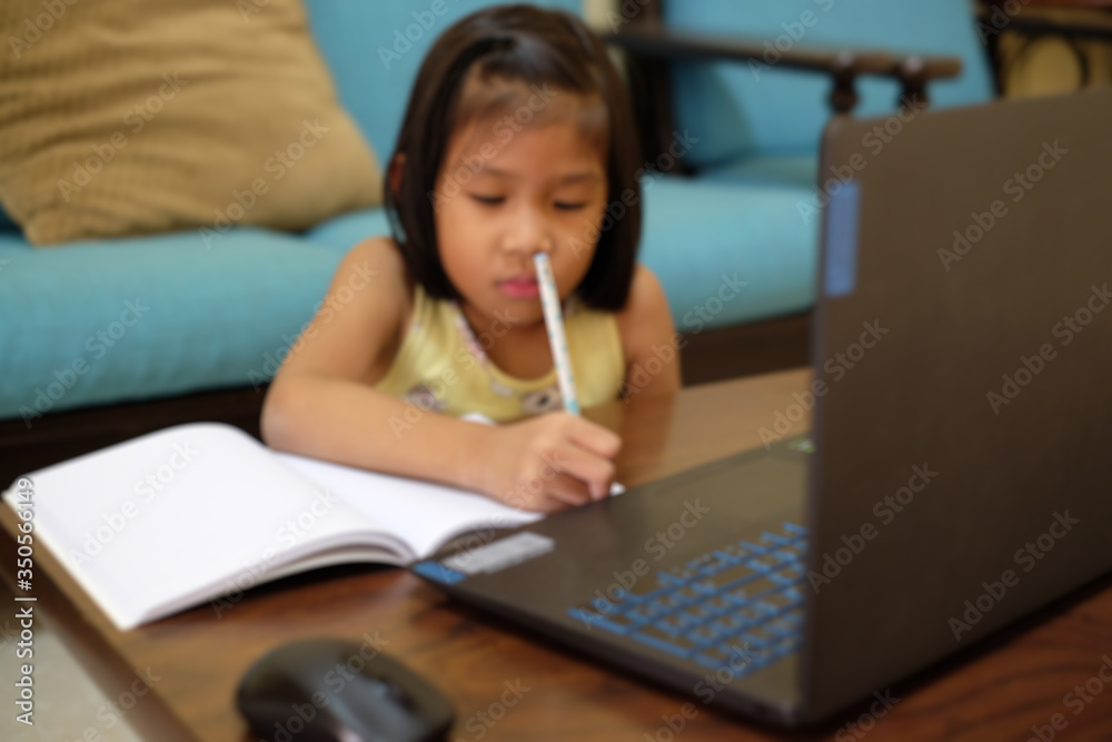 Thai girl in online learning class at home during the COVID-19 situation. Student writing the book and learning form notebook during quarantine. Blurred focus. Online education, home school concept. Thai girl in online learning class at home during the COVID-19 situation. Student writing the book and learning form notebook during quarantine. Blurred focus. Online education, home school concept.