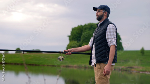 A young bearded man fishing on a lake, a fisherman holding a fishing rod in his hands